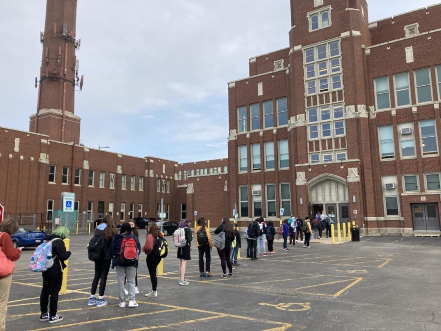 Students wait to enter the building at Door M. Upon entering, security officers verify that they have completed CPS health screener, and a nurse takes their temperature.