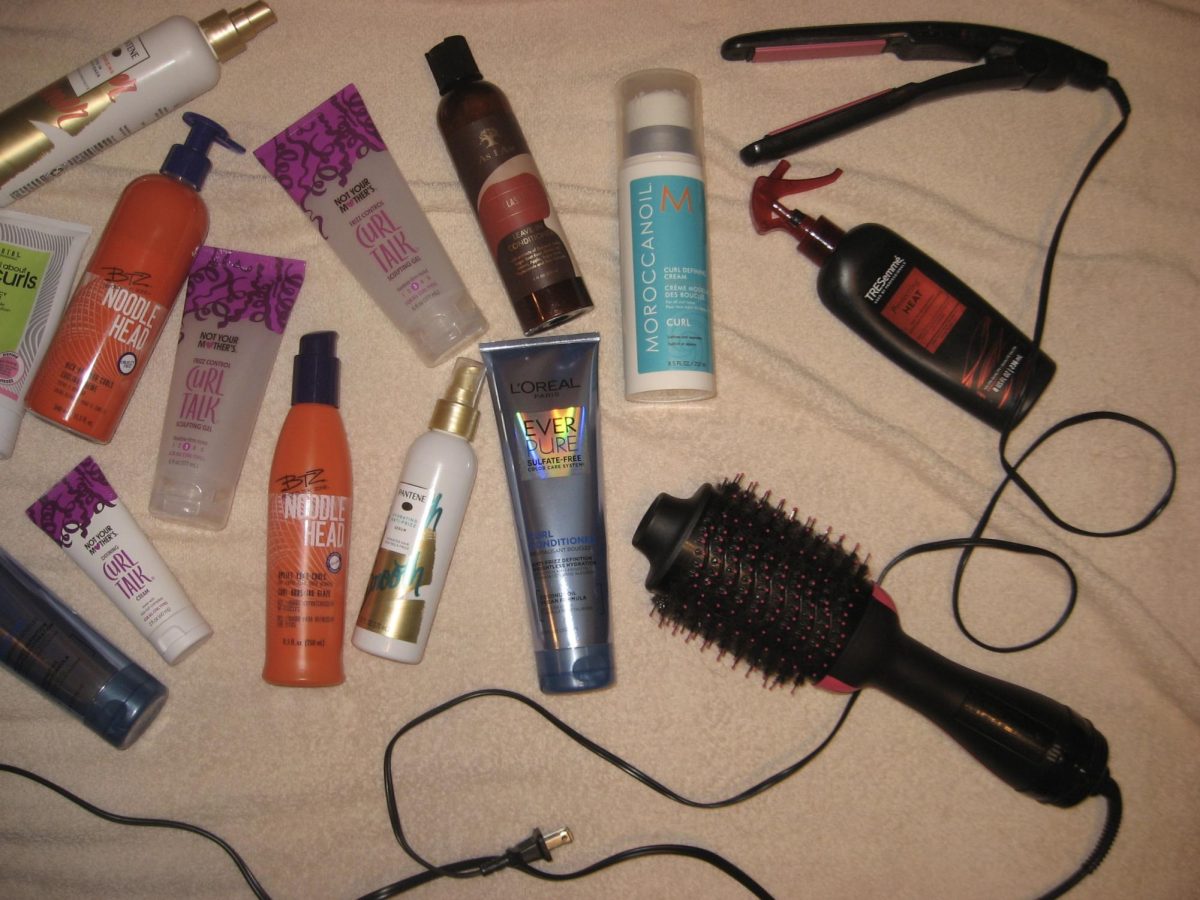 A chaotic array of curly hair products alongside heat tools used for straightening hair. 
